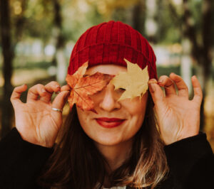 Femme portant une tuque rouge qui se cache les yeux avec des feuilles d’automne