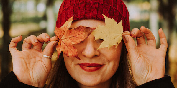 Femme portant une tuque rouge qui se cache les yeux avec des feuilles d’automne