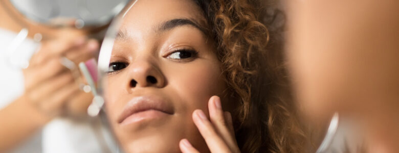 Jeune fille qui regarde sa peau dans un petit miroir rond